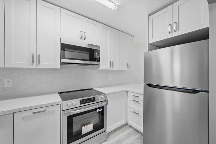 Renovated modern kitchen featuring white shaker cabinetry, stone countertops, stainless steel appliances, and built-in dishwasher.