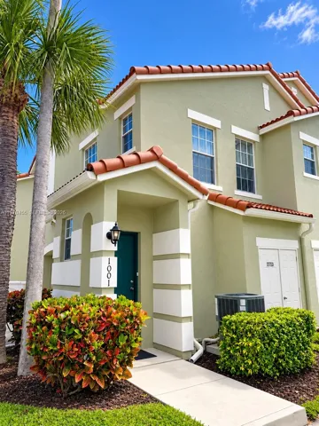 Two-story exterior featuring stucco siding, decorative corner quoins, a terracotta-style tiled roof, and an arched entryway with a wall-mounted coach light