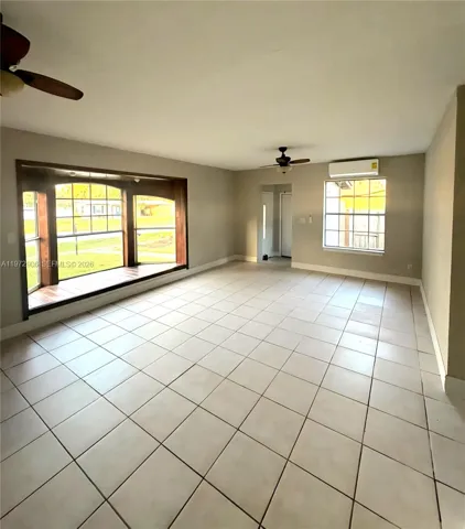 Interior space featuring large bay windows with wood trim, ceramic tile flooring, two ceiling fans, and a wall-mounted climate control unit