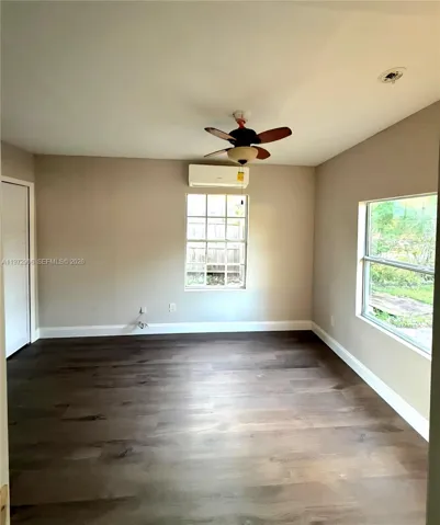 Interior space featuring wood-finish flooring, a wall-mounted ductless mini-split HVAC unit, a ceiling fan with integrated lighting, and multiple windows