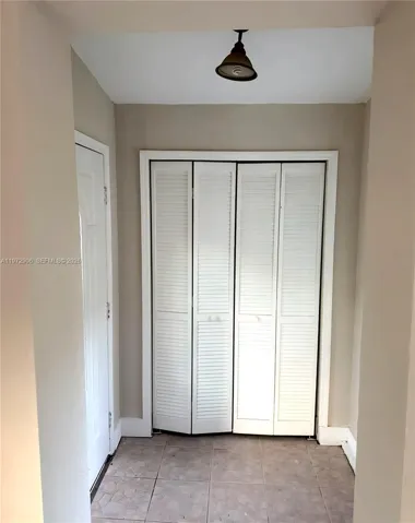 Four-panel white louvered bifold closet doors, neutral wall finish, stone-tile flooring, and a flush-mount light fixture