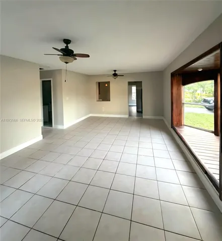 Spacious room featuring large-format tile flooring, dual ceiling fans, a wood-trimmed bay window with a built-in seat, and a pass-through opening