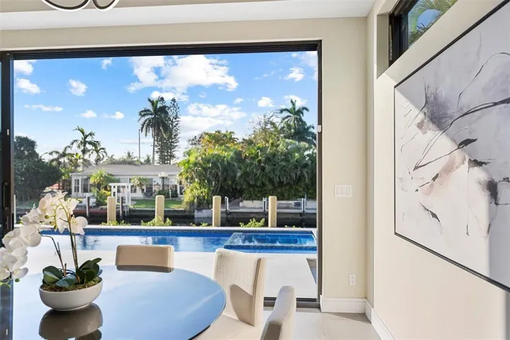 Expansive glass doors open to a private pool and waterway, featuring a tiled pool deck and lush tropical landscaping