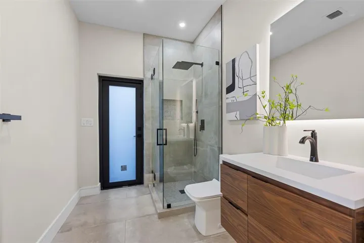 Floating wood-finish vanity with an integrated rectangular sink, matte black faucet, and backlit mirror