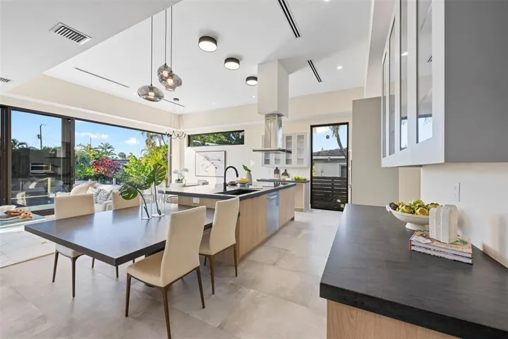 Expansive sliding glass doors, contemporary kitchen island with seating, dark countertops, light wood-finish cabinetry, and recessed lighting