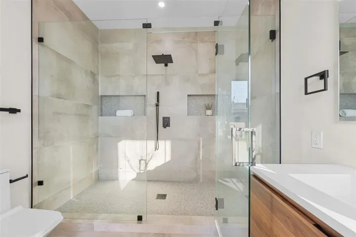 Glass-enclosed shower with a rainfall showerhead, integrated tiled niches, and a mosaic tile floor