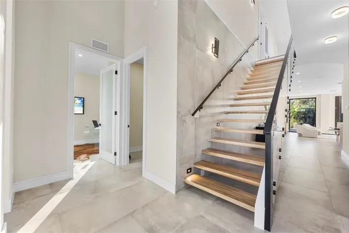 Modern floating staircase with wood-finish treads and a glass railing with a black metal handrail