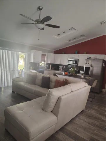 Vaulted ceilings with integrated recessed lighting, wood-finish flooring, white cabinetry, stainless steel appliances, and a central ceiling fan