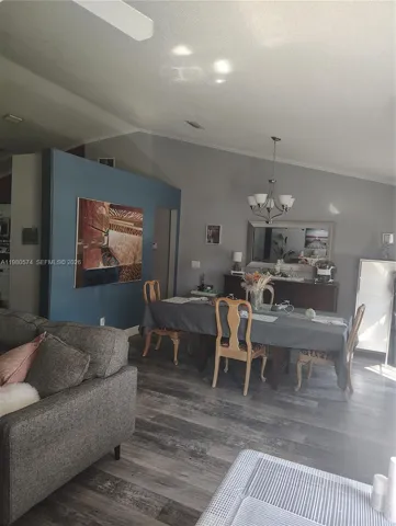 Vaulted ceilings, wood-finish flooring, accent wall, and multi-arm chandelier lighting