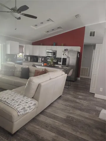Open-concept area featuring vaulted ceilings, skylights, wood-finish flooring, white cabinetry, and stainless steel kitchen appliances