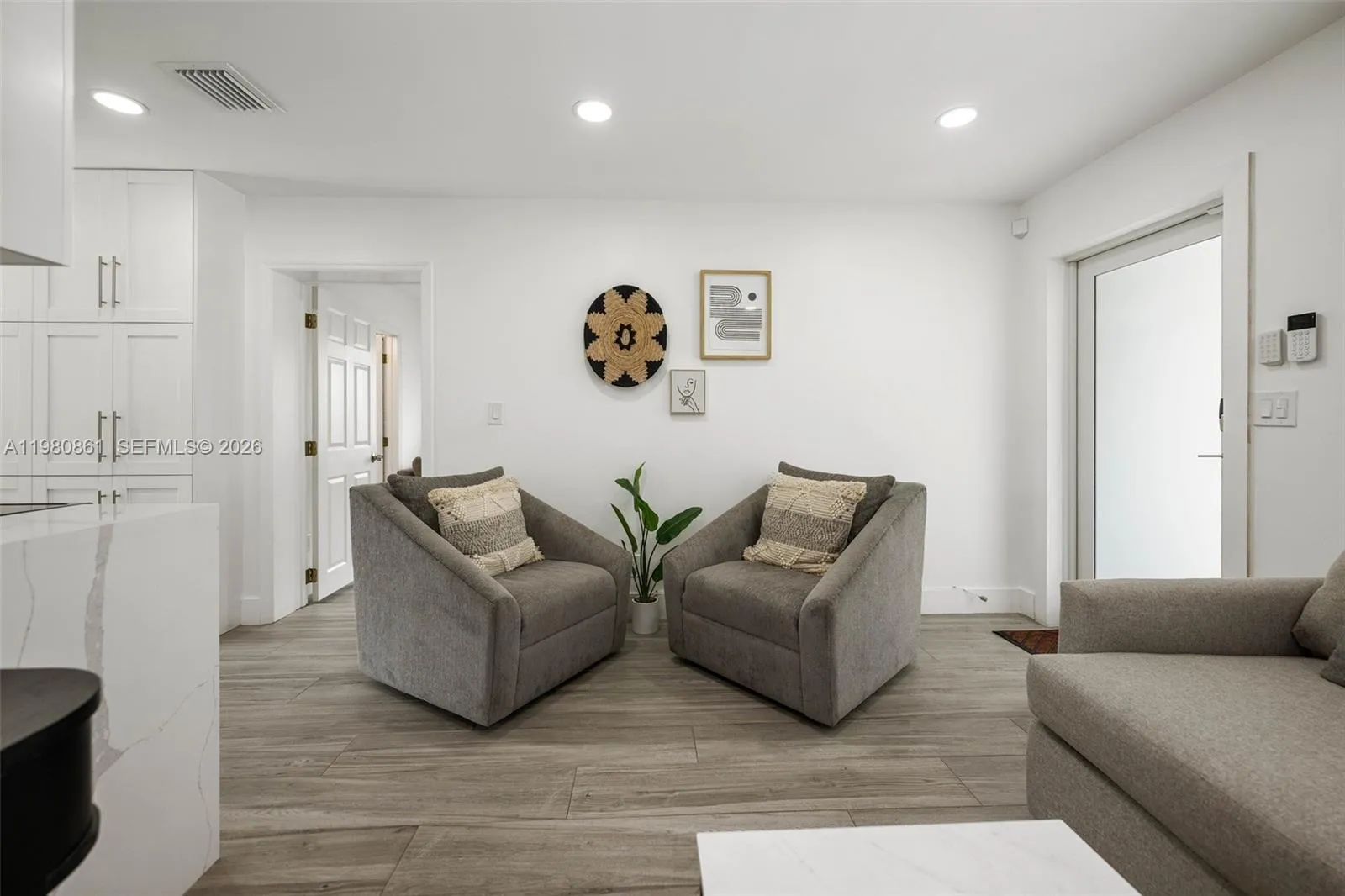 Sophisticated living area designed with balance and elegance, featuring wide-plank flooring, recessed lighting, and a refined neutral palette. Plush seating, curated wall art, and clean architectural lines create a serene, gallery-inspired setting that feels both inviting and elevated—perfect for relaxed living or intimate entertaining.