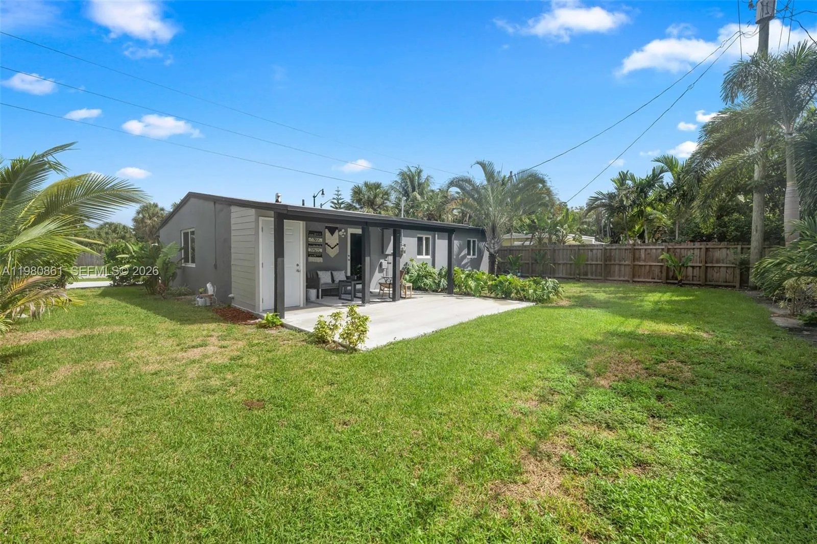 Expansive private backyard retreat offering effortless indoor-outdoor living and endless entertaining potential. Lush green lawn, mature tropical landscaping, and a covered patio create a serene setting ideal for alfresco dining, relaxing evenings, or future customization—perfectly capturing the essence of refined South Florida living.