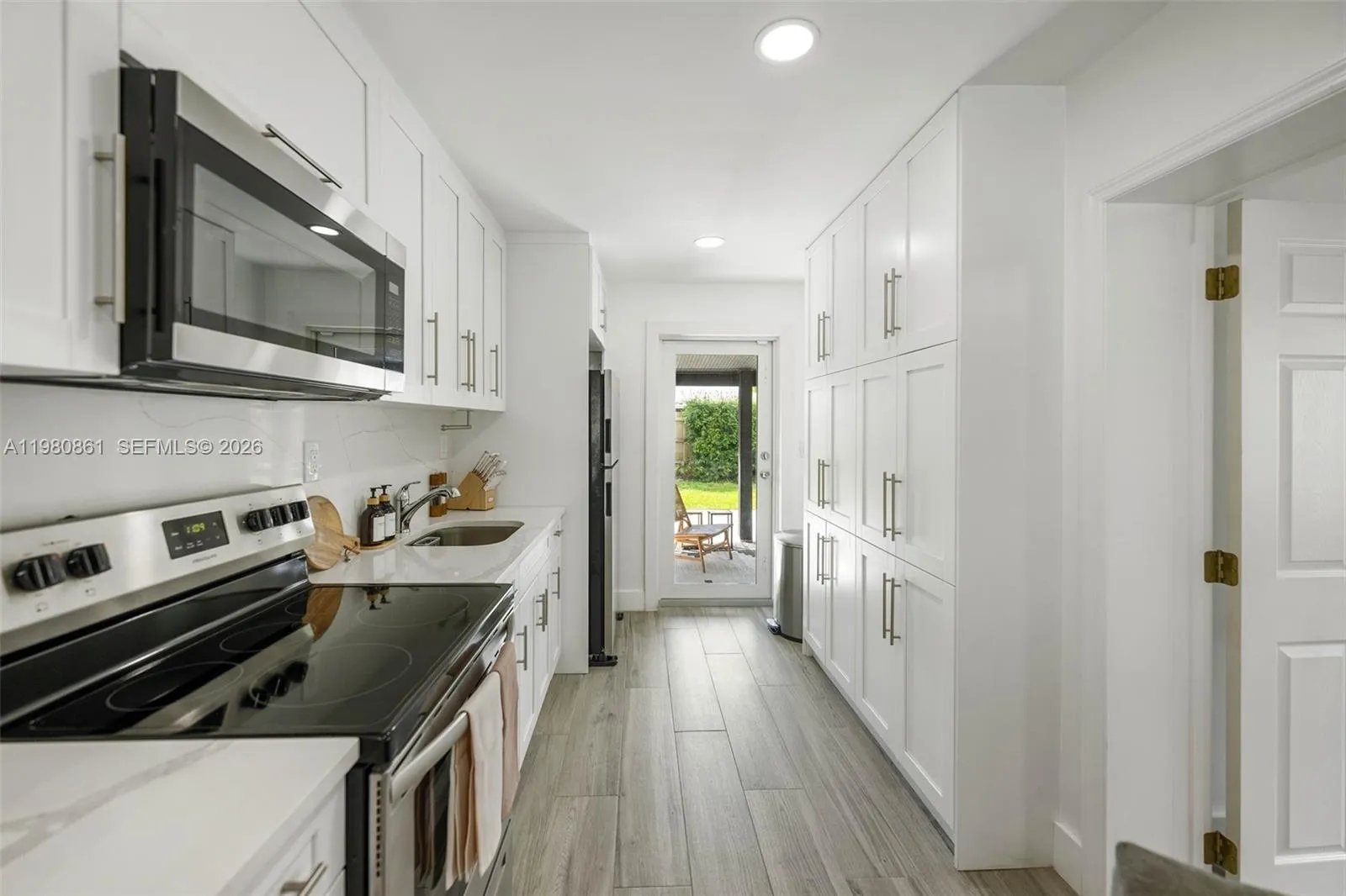 Bright, open-concept kitchen designed for effortless indoor-outdoor living, featuring expansive white shaker cabinetry, quartz countertops, and sleek stainless-steel appliances. Recessed lighting and wide plank flooring enhance the clean, modern aesthetic, while direct access to the backyard creates a seamless flow—perfect for entertaining, everyday living, and enjoying the South Florida lifestyle.