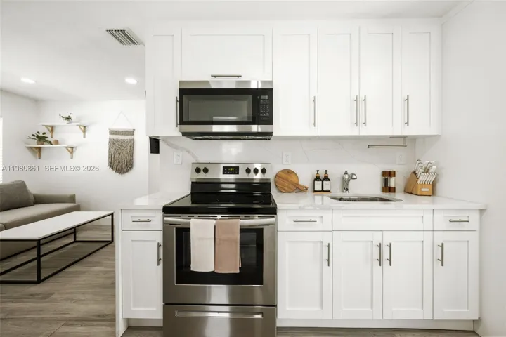 Designer kitchen showcasing crisp white shaker cabinetry, quartz countertops, and stainless-steel appliances seamlessly integrated into an open-concept layout. Thoughtfully styled with refined finishes, warm wood accents, and modern lighting, this elegant culinary space blends timeless sophistication with everyday functionality—perfect for both entertaining and elevated daily living.