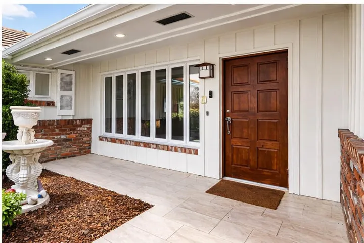 Covered front entrance featuring double doors, tiled entryway, and decorative landscaping.