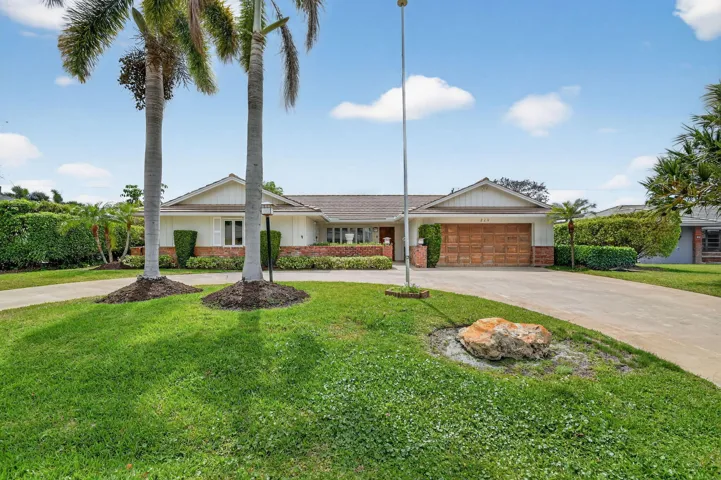 Front yard view highlighting manicured lawn, palm trees, and driveway leading to the home.