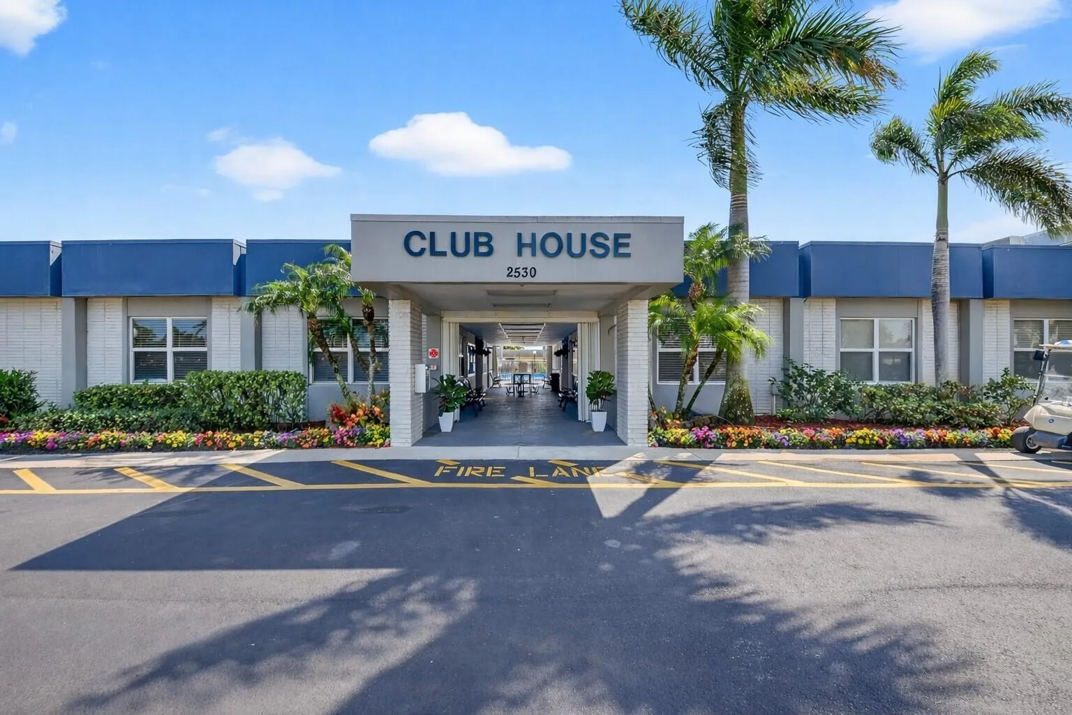 Beautifully maintained clubhouse with vibrant landscaping & palm trees.