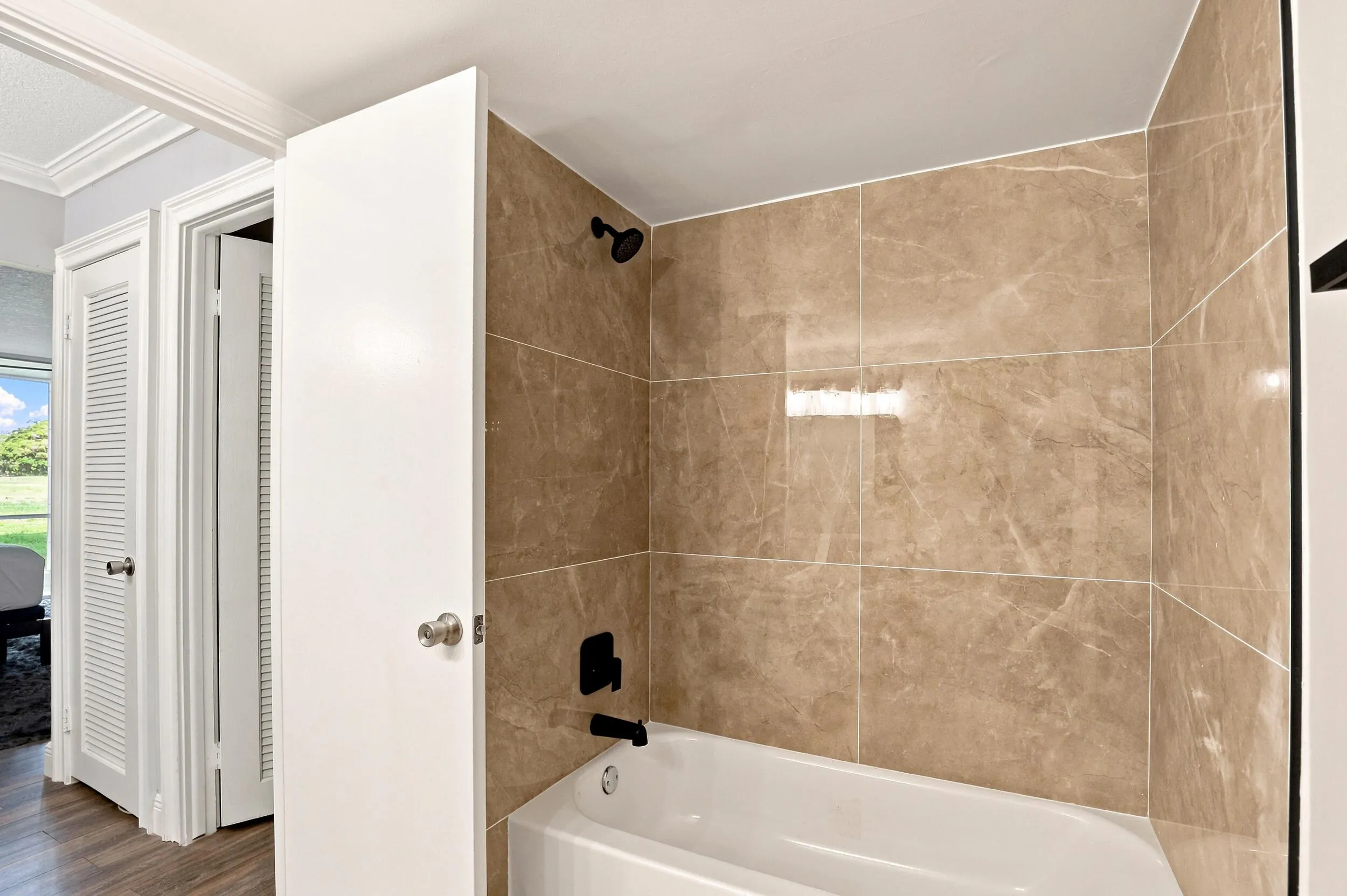 Beautifully renovated with a clean, modern design, the primary ensuite bathroom showcases a stylish new vanity with matte black fixtures, updated lighting, and a contemporary mirror. The spacious tub and shower combination is surrounded by elegant floor to ceiling tile, creating a sophisticated, spa inspired retreat that blends timeless finishes with everyday functionality.