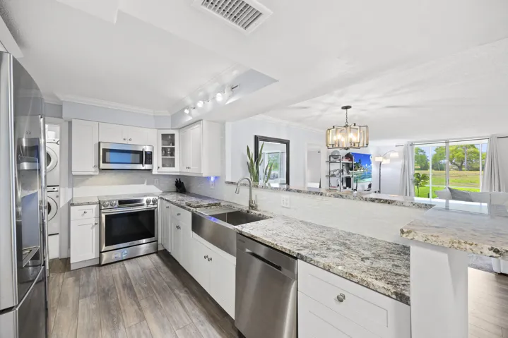 A thoughtfully updated kitchen designed to blend style and functionality, featuring sleek cabinetry, stainless steel appliances, and beautiful granite countertops that offer both durability and elegance. The open pass-through to the main living area keeps you connected while entertaining, while the farmhouse sink and ample prep space make everyday living effortless. Just beyond, a dedicated laundry area adds an extra layer of convenience to this well-designed space.