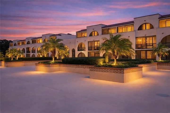 The property features a multi-story building with arched windows and balconies, complemented by decorative planters with palm trees and manicured hedges