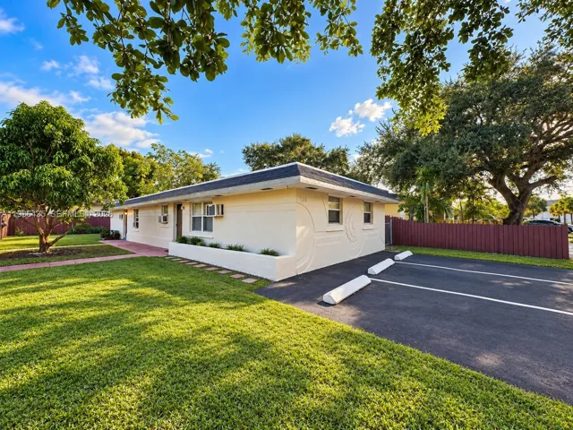 Single-story stucco exterior featuring integrated decorative masonry patterns, asphalt parking area, built-in concrete planters, and mature landscaping