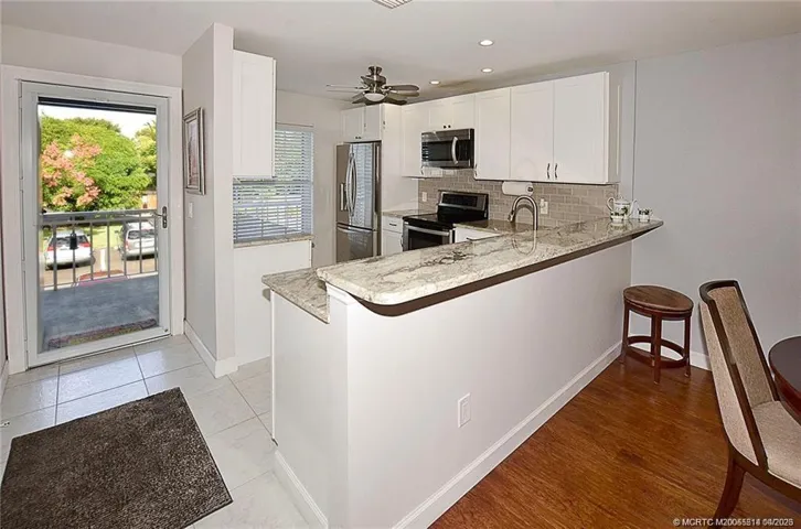 Updated kitchen featuring white shaker cabinetry, granite countertops, stainless steel appliances, tile backsplash, and a spacious breakfast bar perfect for additional seating