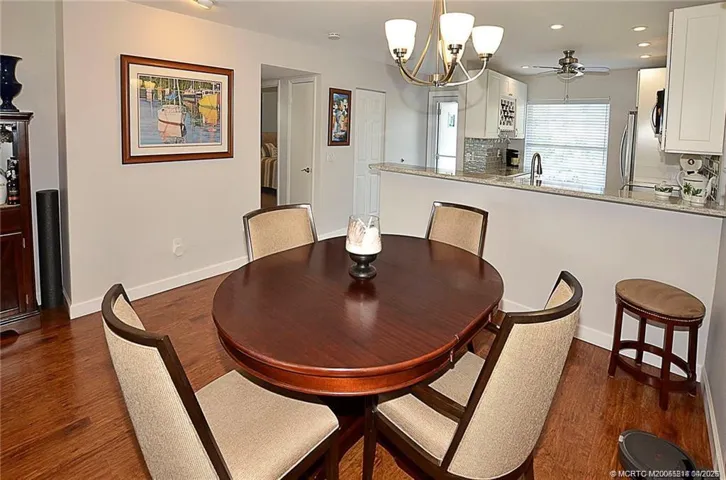 Spacious dining area with wood-look flooring opens to a beautifully updated kitchen featuring granite countertops, tile backsplash, bar seating, and recessed lighting.