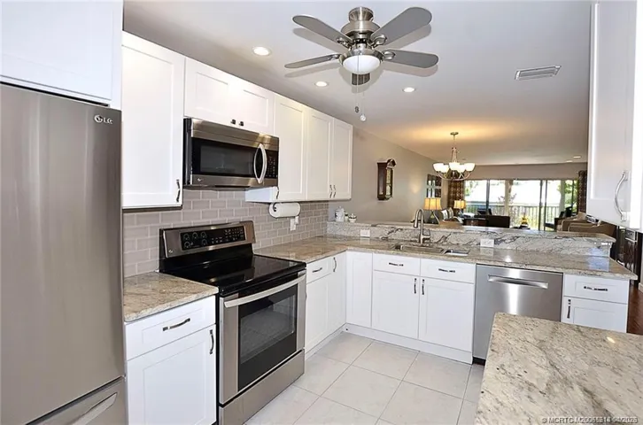 This stunning kitchen is the heart of the home, featuring expansive granite counters, modern white cabinetry, and an open layout that flows seamlessly into the living space and out to the lanai—perfect for entertaining.
