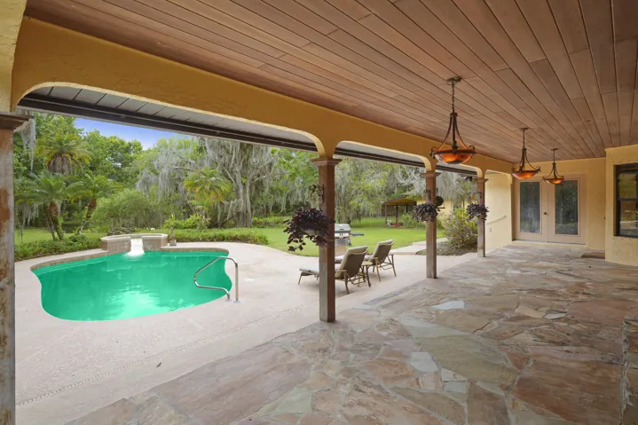 Elegant covered outdoor entertaining area with stone flooring and designer chandeliers.