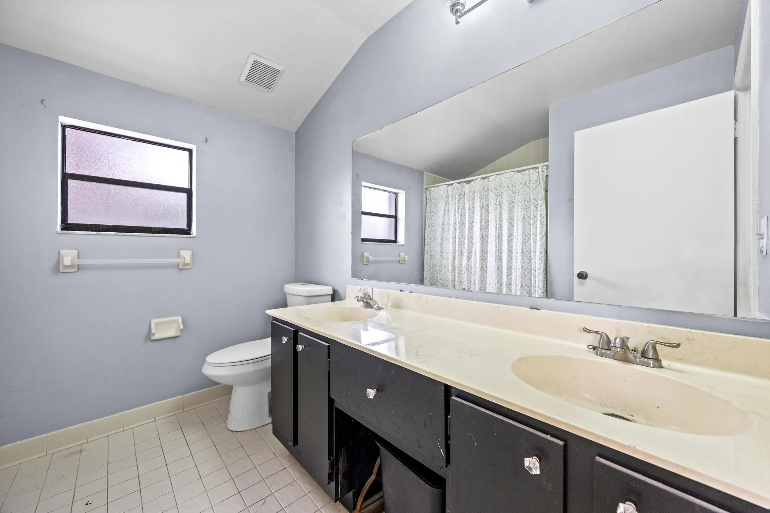 Spacious primary bathroom featuring a long dual-sink vanity with ample counter space, perfect for everyday functionality. The layout includes a walk-in shower with sliding glass enclosure and a window for natural light, creating a bright and airy feel. A great opportunity to personalize and update to your own style while enjoying the generous footprint.v