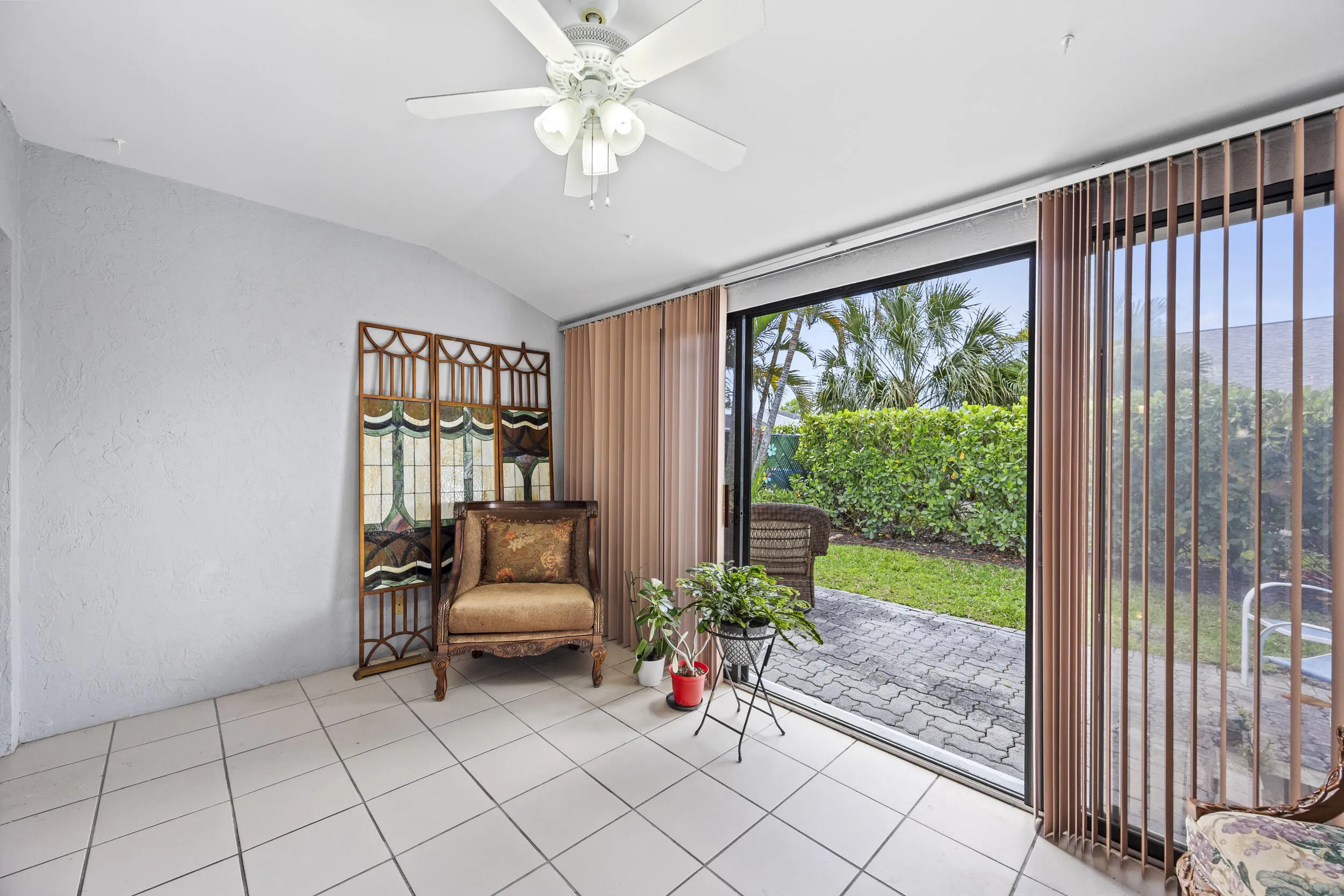 Inviting covered patio offering a comfortable indoor-outdoor living experience, complete with durable tile flooring and expansive sliding glass doors that fill the space with natural light. This versatile area is perfect for relaxing, entertaining, or enjoying morning coffee while overlooking the private, lushly landscaped backyard.