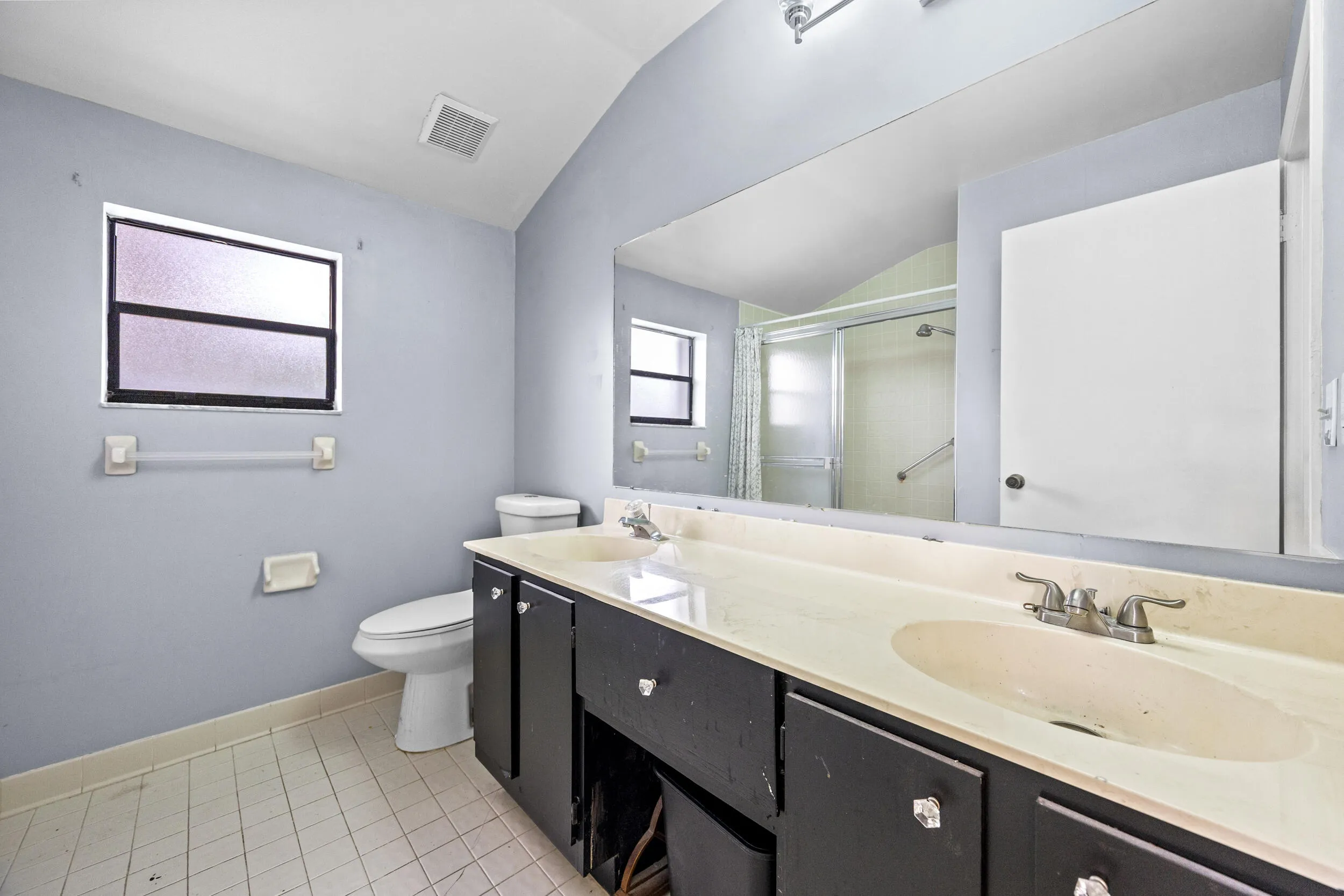 Spacious primary bathroom featuring a long dual-sink vanity with ample counter space, perfect for everyday functionality. The layout includes a walk-in shower with sliding glass enclosure and a window for natural light, creating a bright and airy feel. A great opportunity to personalize and update to your own style while enjoying the generous footprint.