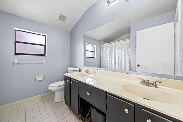 Spacious primary bathroom featuring a long dual-sink vanity with ample counter space, perfect for everyday functionality. The layout includes a walk-in shower with sliding glass enclosure and a window for natural light, creating a bright and airy feel. A great opportunity to personalize and update to your own style while enjoying the generous footprint.v