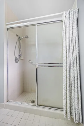 Spacious primary bathroom featuring a long dual-sink vanity with ample counter space, perfect for everyday functionality. The layout includes a walk-in shower with sliding glass enclosure and a window for natural light, creating a bright and airy feel. A great opportunity to personalize and update to your own style while enjoying the generous footprint.
