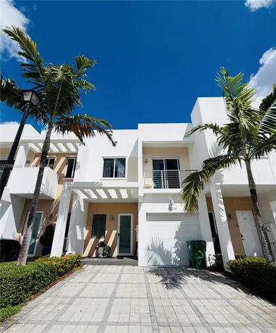 Modern multi-story exterior featuring a white stucco facade, private balcony with metal railing, integrated garage, and a paved driveway