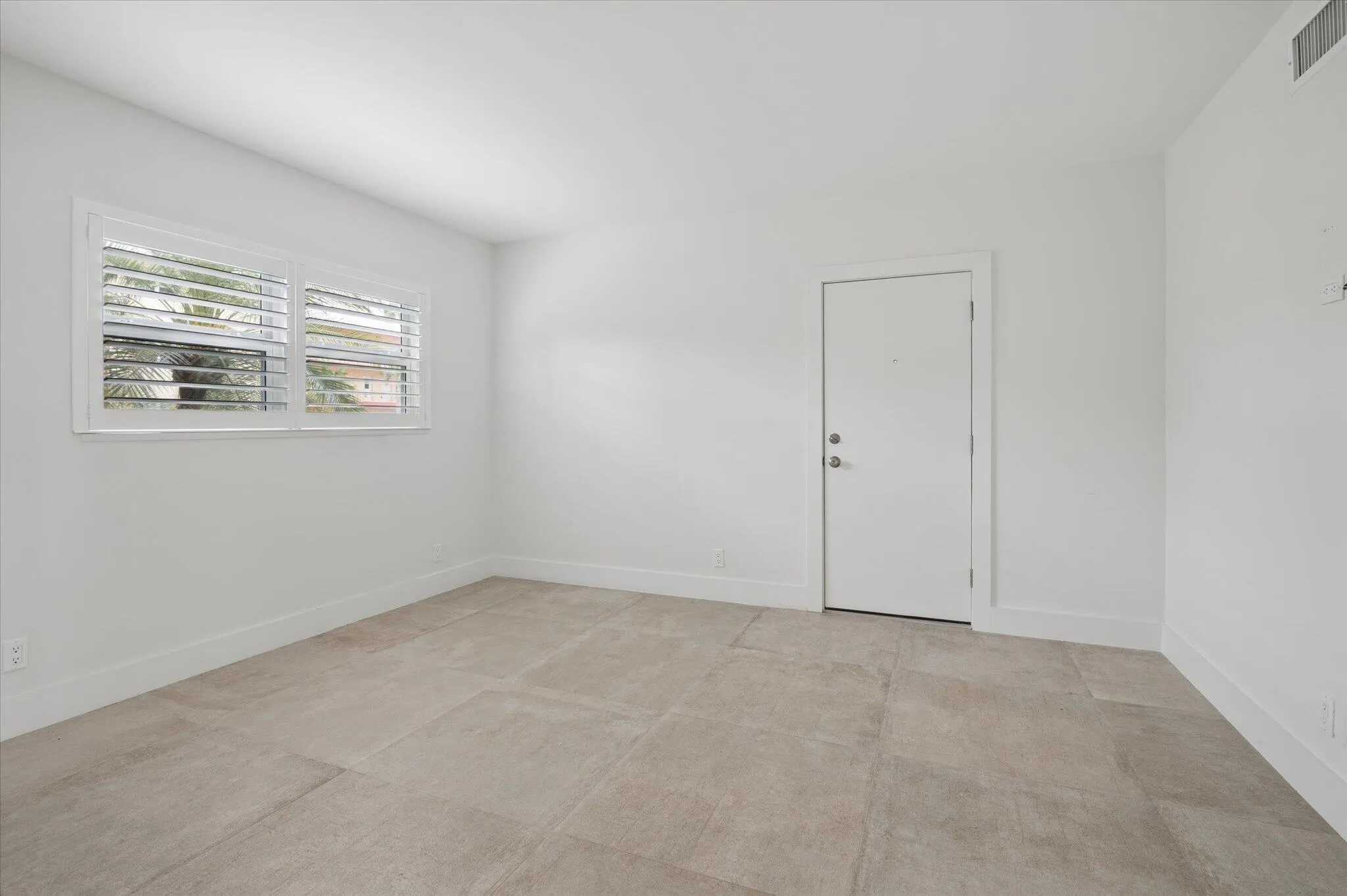 Bright and airy bedroom featuring plantation shutters and neutral tile flooring throughout.