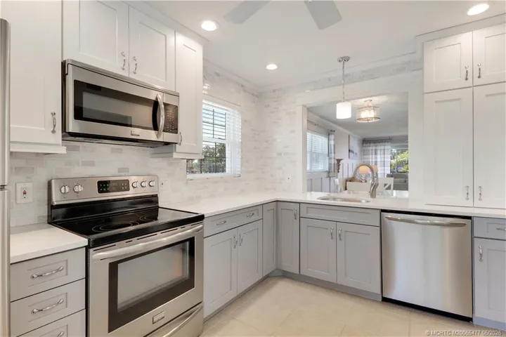 Beautifully renovated kitchen featuring soft gray shaker cabinetry, quartz countertops, tiled backsplash, stainless steel appliances, recessed lighting, and an open pass-through design perfect for entertaining.