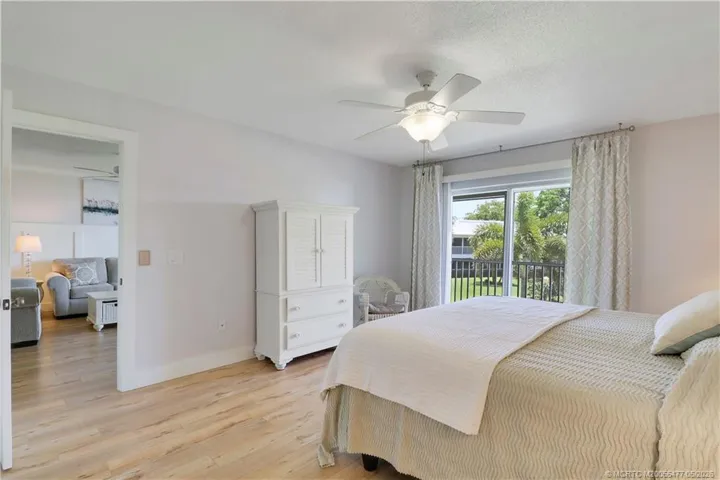 Relaxing primary bedroom retreat with private lanai access, beautiful natural light, wood-look flooring, and serene views of the lush grounds and waterways.
