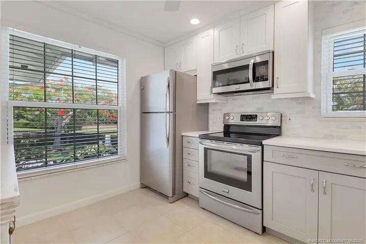 Light and bright remodeled kitchen with abundant shaker cabinetry, quartz counters, stainless appliances, custom tile backsplash, recessed lighting, and neutral coastal finishes throughout.