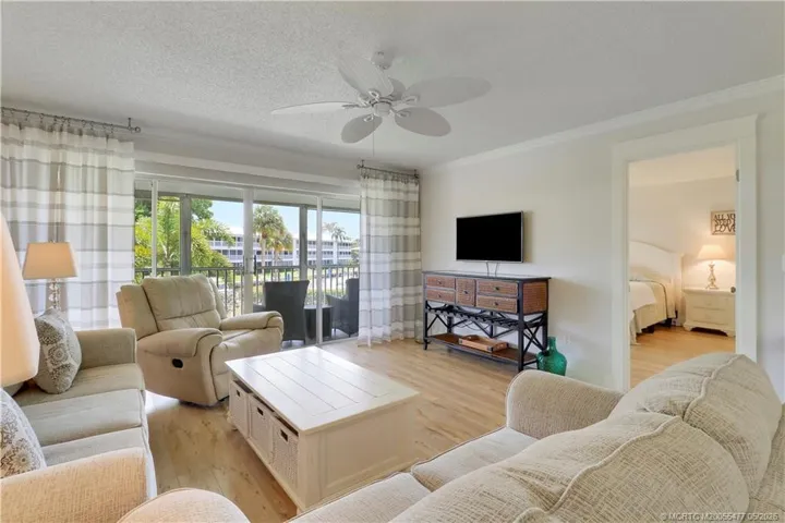 Spacious light-filled living area with luxury vinyl plank flooring, custom wall detailing, neutral coastal décor, and sliding glass doors opening to the expansive screened lanai.