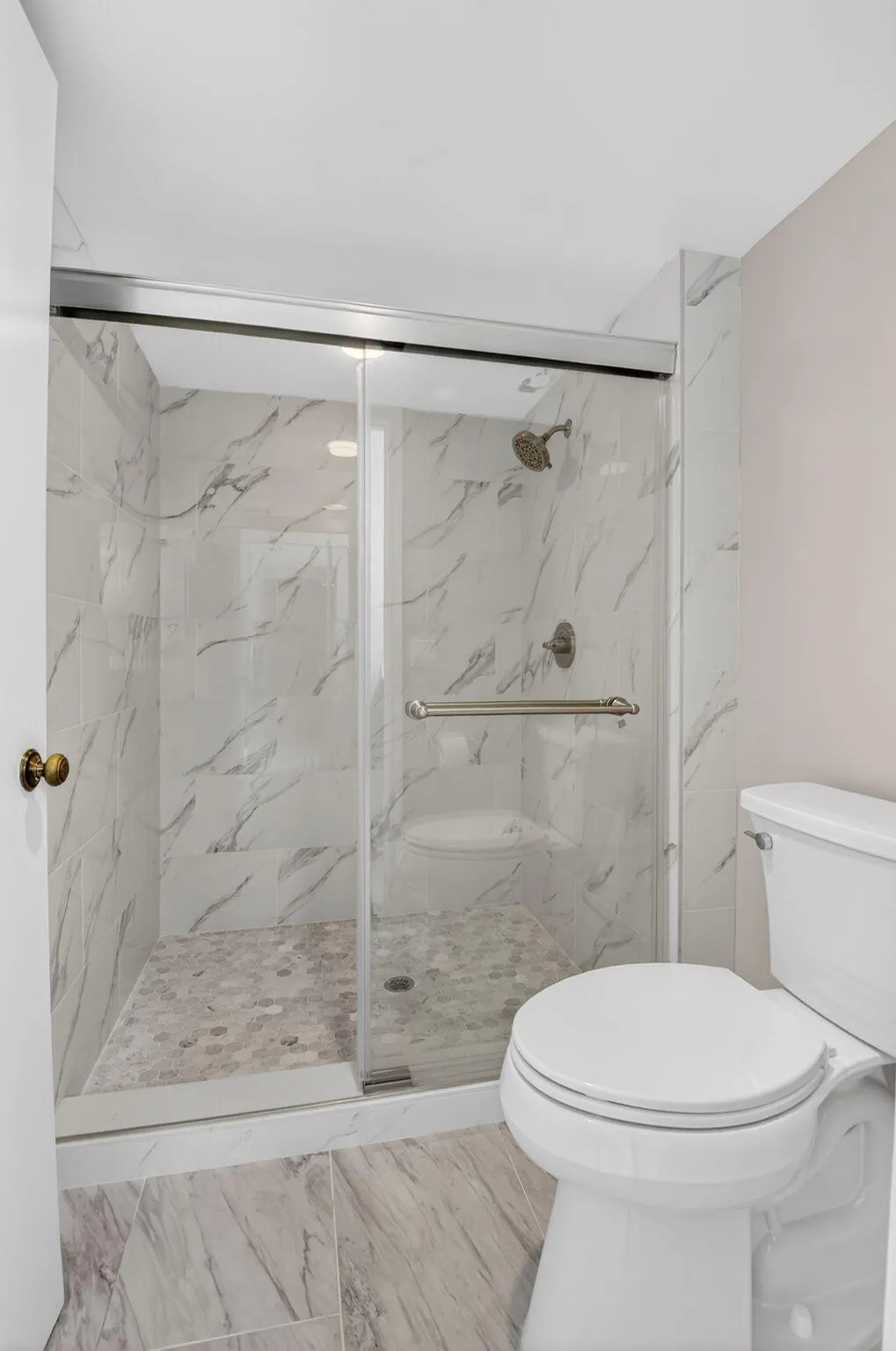 Walk-in shower with glass enclosure, tile surround and convenient grab bar.