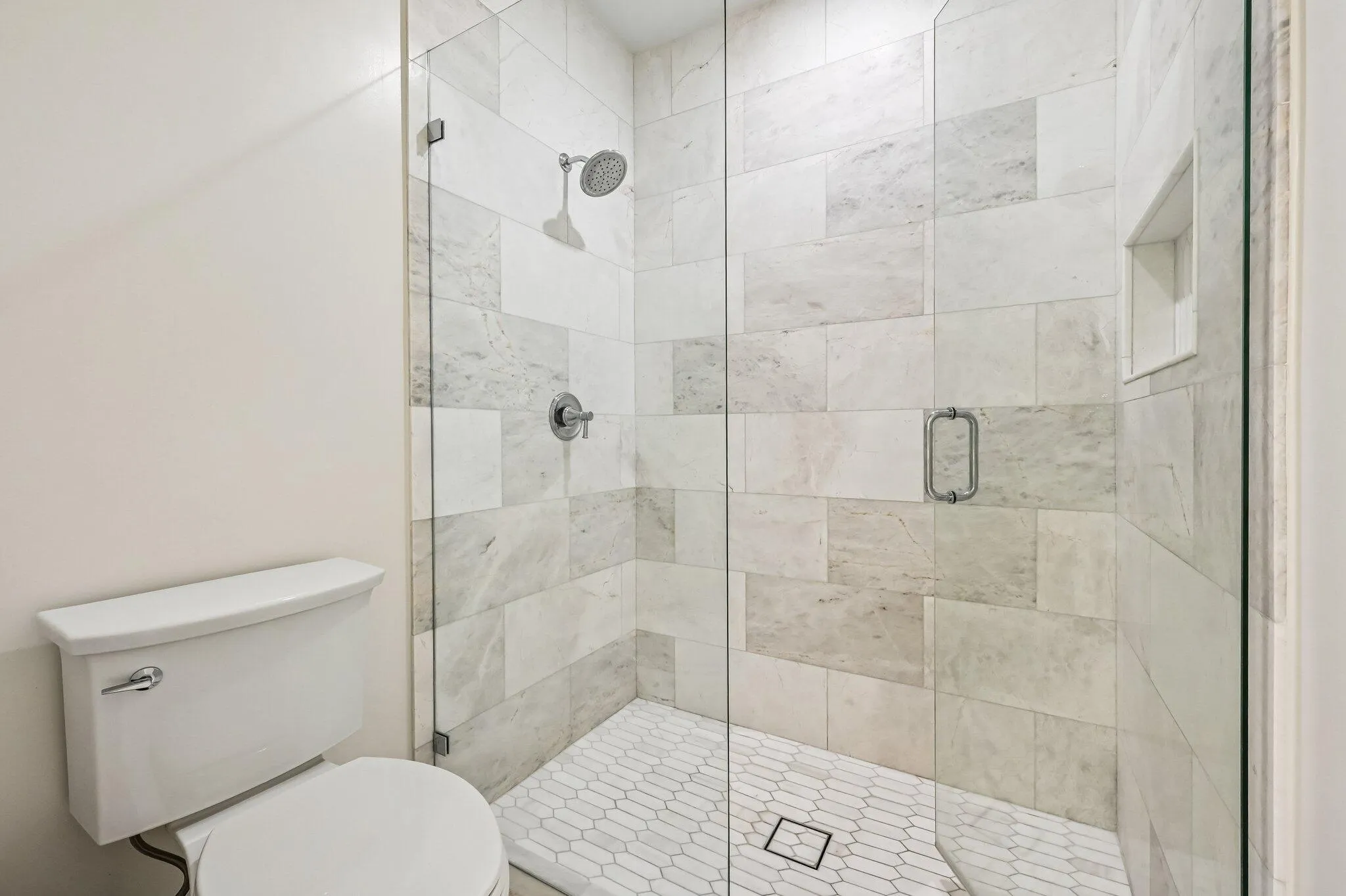 The elegant primary bathroom showcases marble flooring and a beautifully designed glass-enclosed shower, adding a touch of timeless sophistication.
