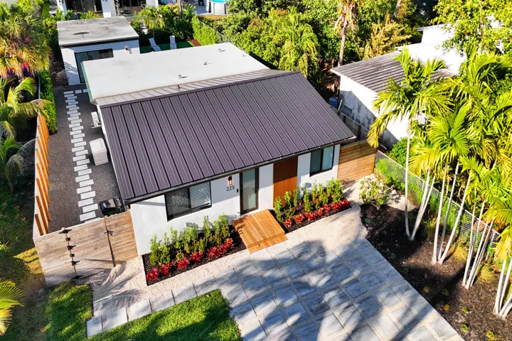 Drone view highlighting the home's modern architecture, metal roof, and beautifully landscaped lot.