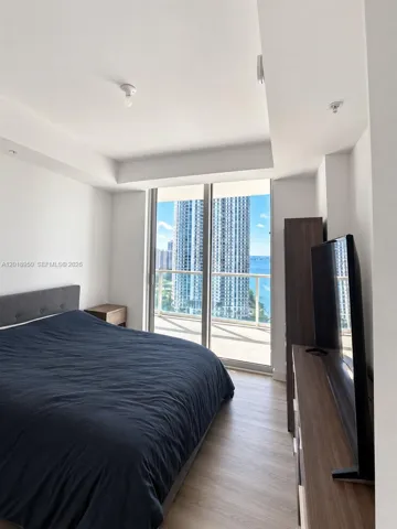 Floor-to-ceiling glass sliding doors, wood-finish flooring, and recessed ceiling detailing, incorporating a balcony with water and urban scenery