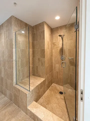 Walk-in shower featuring floor-to-ceiling stone tile, a built-in bench, a glass enclosure, and a chrome hand-held shower fixture