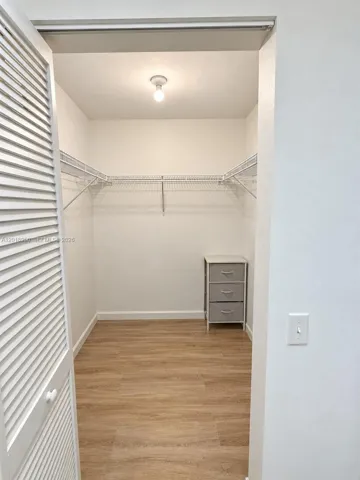 Walk-in closet featuring wood-finish flooring, white louvered bifold doors, and integrated wire shelving