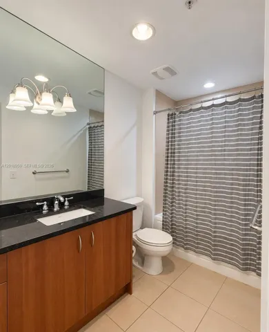 Bathroom featuring a wood-finish vanity with a dark stone countertop, rectangular undermount sink, expansive wall-mounted mirror, and tile flooring