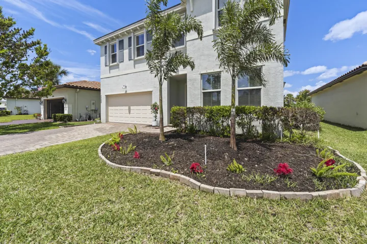 Fresh landscaping, tropical palms, and a paver driveway create an inviting exterior.