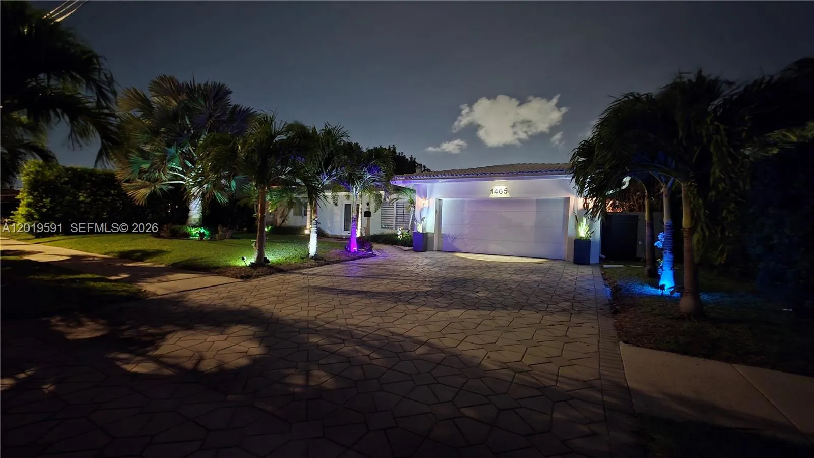 Beautiful illuminated waterfront home exterior showcasing tropical landscaping and luxury nighttime curb appeal.