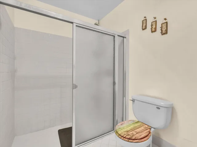 Primary bathroom angle focused on the shower enclosure, toilet area, tile flooring, and neutral wall finishes.